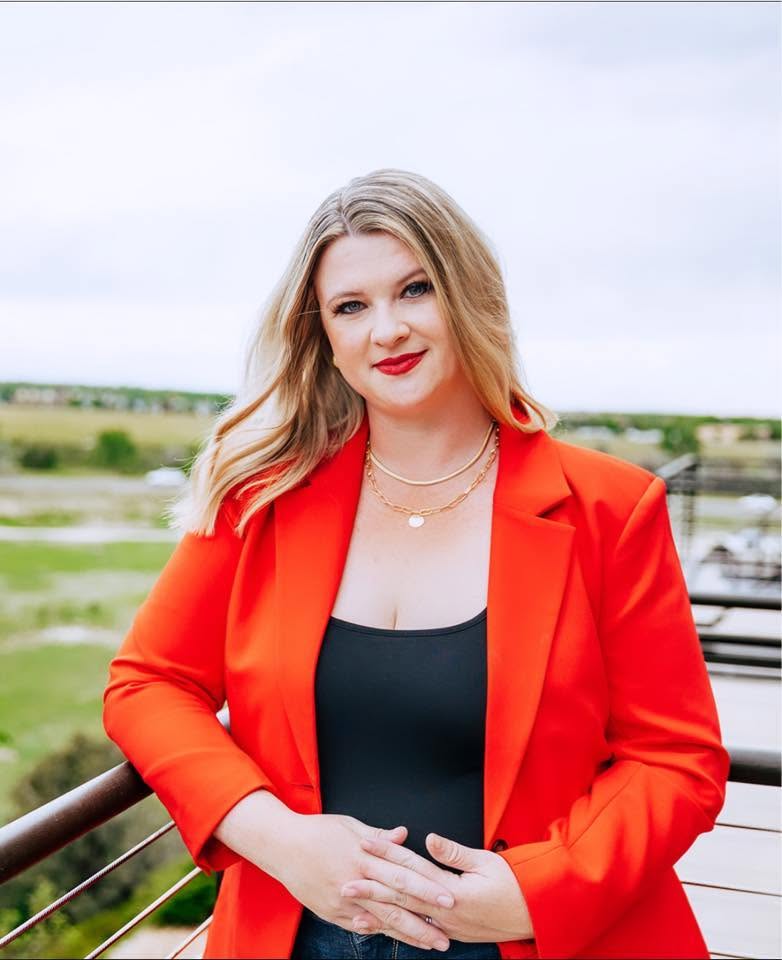 Ashley Heckathorn, Compass Broker Associate and Johnstown Colorado Realtor, in a red blazer with the Colorado prairie behind her